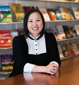 A woman in a black-and-white dress sits in front of a book display